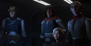 In a scene from Star Wars: The Bad Batch, three adults stand in a dimly lit room and wear gray and tan clothing, while a child sits in the chair in front of them.