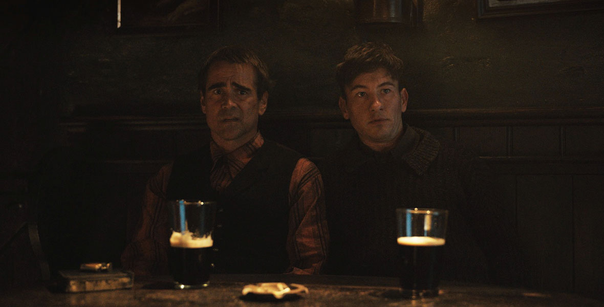Colin Farrell and Barry Keoghan sit in a dimly lit bar. They are seated at a table. Two half-full pints of beer and an ashtray are placed on the table before them.