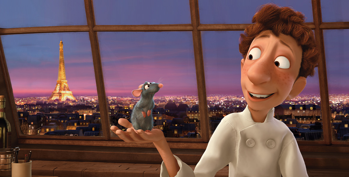 In a scene from Pixar’s Ratatouille, a young man wears a white chef’s coat and holds a gray rat in his outstretch right palm. They stand in front of a large window depicting the Paris skyline.