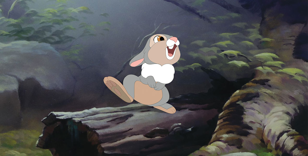 In the forest, Thumper sits smiling atop a small log with his right foot in the air.