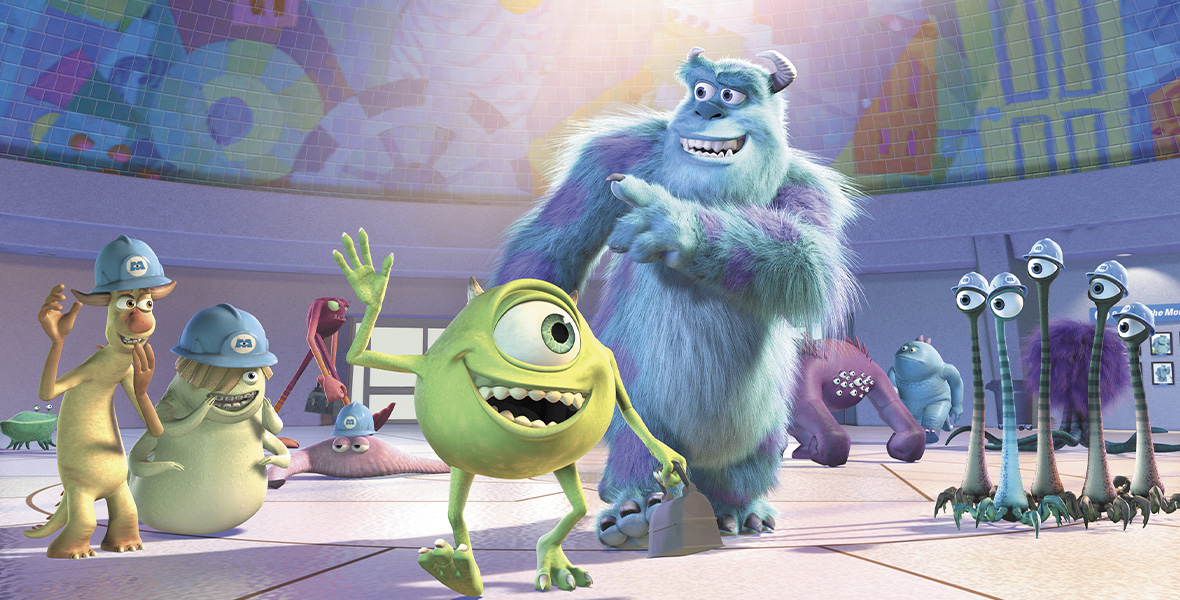 In a scene from Pixar’s Monsters Inc., Mike, a short, green, rotund monster, walks with Sulley, a tall monster with blue and purple fur, through a large warehouse structure.
