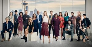 The stars of Grey’s Anatomy pose in front of a window depicting the Seattle skyline.