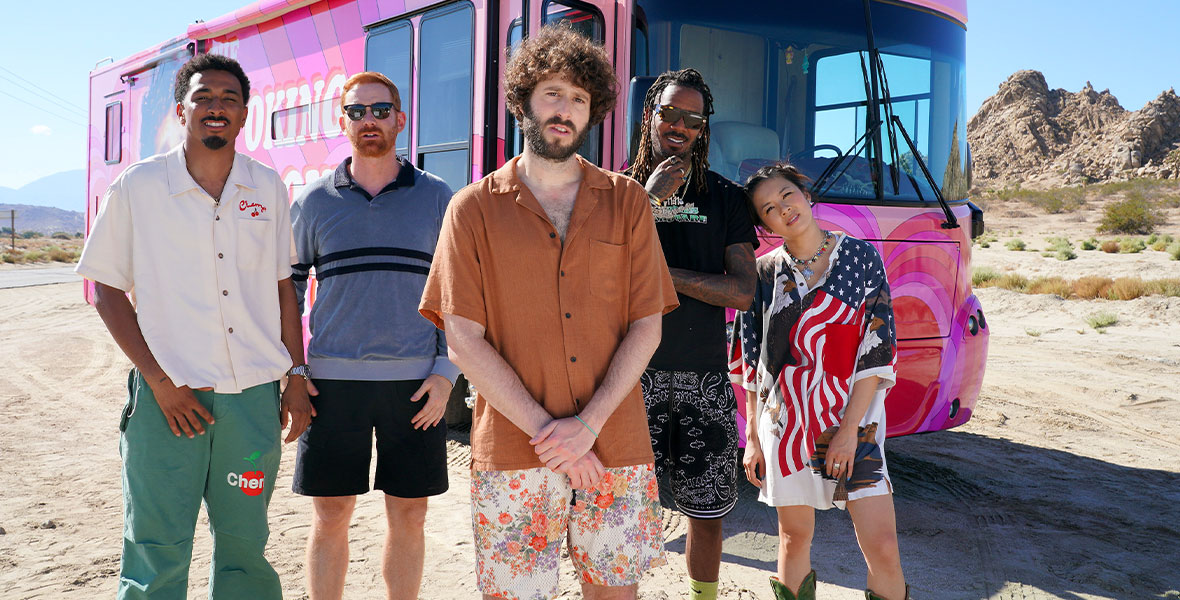 The cast of FX series DAVE pose in front of a pink tour bus parked in the desert.