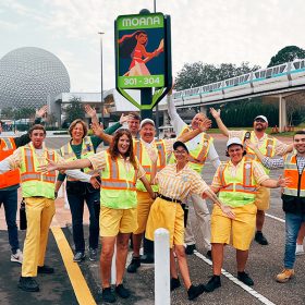 A group of EPCOT cast members pose next to a parking lot sign with the animated character Moana.
