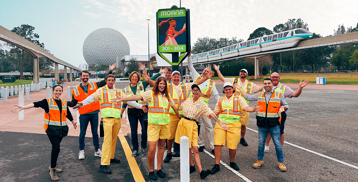 A group of EPCOT cast members pose next to a parking lot sign with the animated character Moana.