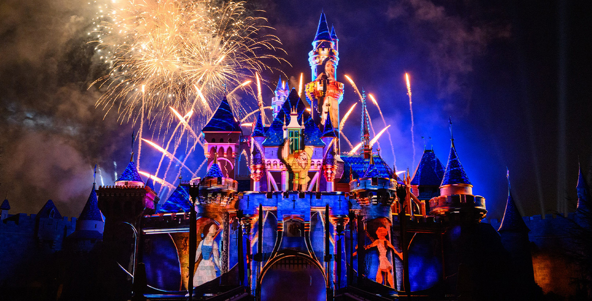 Sleeping Beauty Castle at Disneyland Resort, featuring projections of several Disney films, including Beauty and the Beast, The Hunchback of Notre Dame, and Hercules. Behind the castle, fireworks shoot up into the sky and burst into a brocade shape