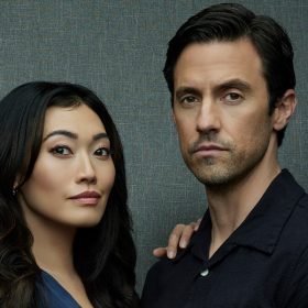 In a promotional photo shoot for The Company You Keep, Catherine Haena Kim stands to the right of Milo Ventimiglia. Kim is wearing a navy blue silk dress and rests her right hand on Ventimiglia’s right shoulder. Ventimiglia is wearing a black button-up shirt and black pants, and his left hand is in his pocket. Neither is smiling.