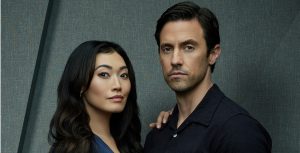 In a promotional photo shoot for The Company You Keep, Catherine Haena Kim stands to the right of Milo Ventimiglia. Kim is wearing a navy blue silk dress and rests her right hand on Ventimiglia’s right shoulder. Ventimiglia is wearing a black button-up shirt and black pants, and his left hand is in his pocket. Neither is smiling.