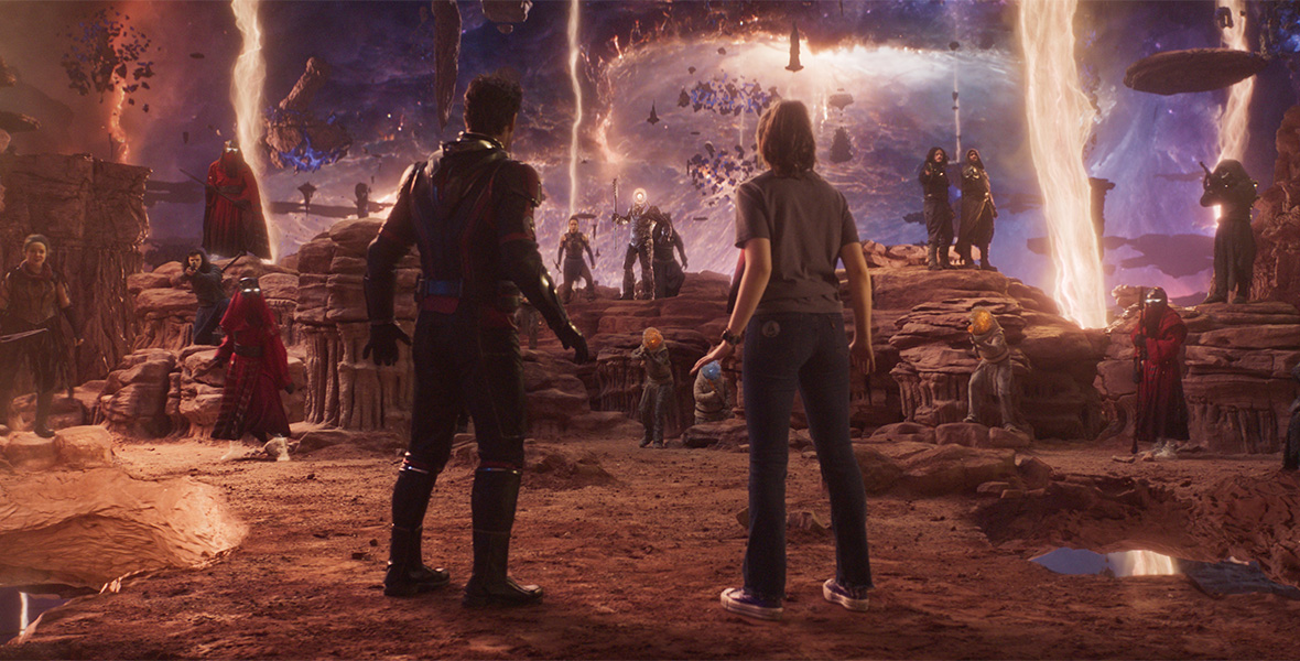 Scott and Cassie stand with their backs to the camera, facing several beings in the Quantum Realm. Some resemble humans while others appear alien. They almost all have their weapons raised toward Scott and Cassie. Bolts of light strike down from a purple sky, which swirls with pieces of rock and debris.
