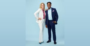 Ali Wentworth wears a white suit, a pink top with a floral print, and blue pumps. She has her right arm on her hip and left arm on Dr. Adolph Brown’s right shoulder. Dr. Brown is wearing a navy suit, a blue shirt, a pink pocket square, and black dress shoes with gold buckles. They are smiling and posing against a blue backdrop.