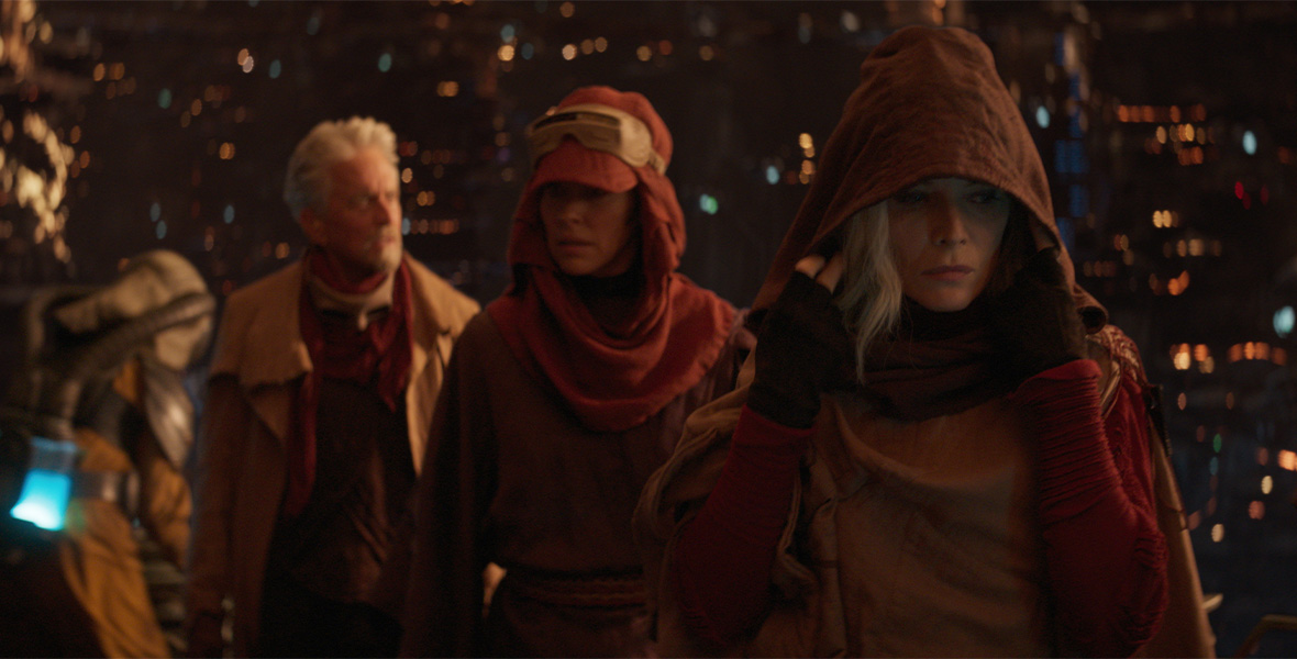 In a scene from Ant-Man and The Wasp: Quantumania, Dr. Hank Pym (left), Hope vVan Dyne/Wasp (center), and Janet Van Dyne/Wasp (right) walk in a single-file line through the Quantum Realm. They are disguising themselves in earth-tone outfits