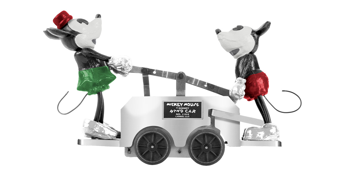 A replica of the Lionel Trains 1934 handcar, featuring Minnie Mouse in a red hat and green skirt and Mickey Mouse in red trousers. Both are operating the platinum-colored handcar together.