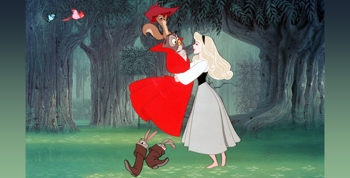 A view of Princess Aurora dancing in the forest in the animated film Sleeping Beauty. She waltzes with an owl, who’s wearing a red cloak. A squirrel sits atop the owl’s head, holding a red hat up, while two rabbits stand on the grass below, each inside a brown boot. Two birds watch nearby. Aurora has long, blond curls with a black headband and wears a gray dress.