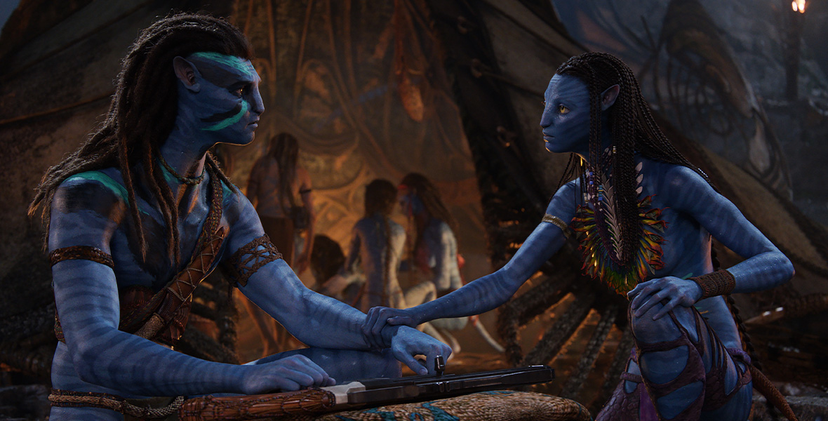 In an image from Avatar: The Way of Water, Jake Sully (portrayed by Sam Worthington) and Neytiri (portrayed by Zoe Saldaña) are talking to one another, while members of their family are seen behind them. They are looking intently at one another.