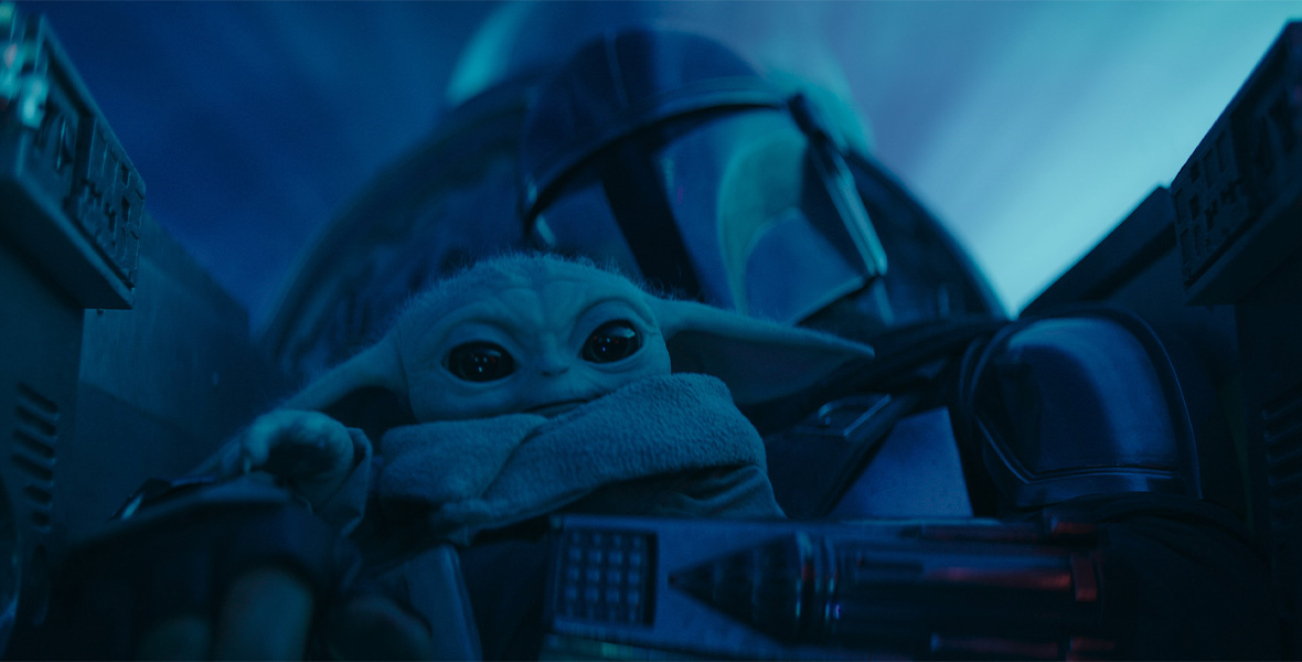 In a scene from The Mandalorian, Grogu sits in The Mandalorian’s lap as he pilots a ship. Because they are traveling at light speed, the ship is awash in blue light.