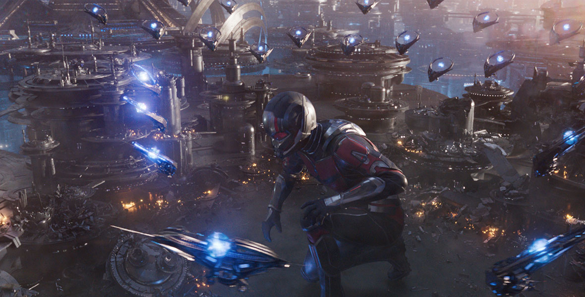 Ant-Man, played by Paul Rudd, has grown more than six times his normal size. He is crouching down on one knee and is surrounded by dozens of flying ships.