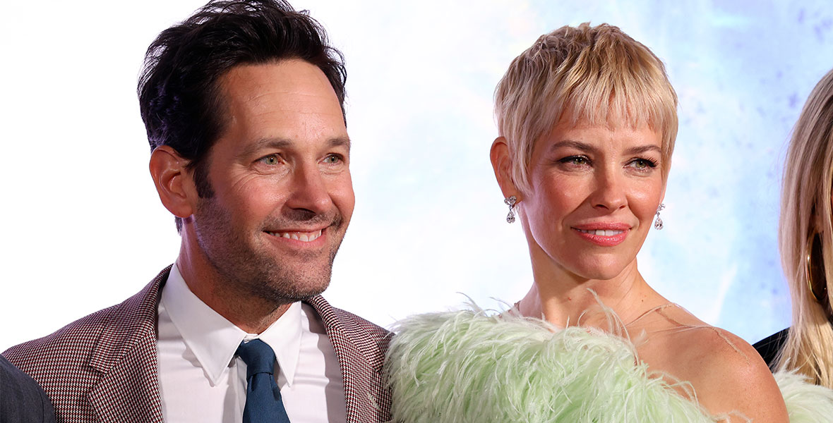 Paul Rudd and Evangeline Lilly pose for a photo. Rudd is smiling and has on a brown checkered suit with a navy-blue tie. Lilly is has a blond pixie cut and is wearing a feathered mint green sleeveless dress.