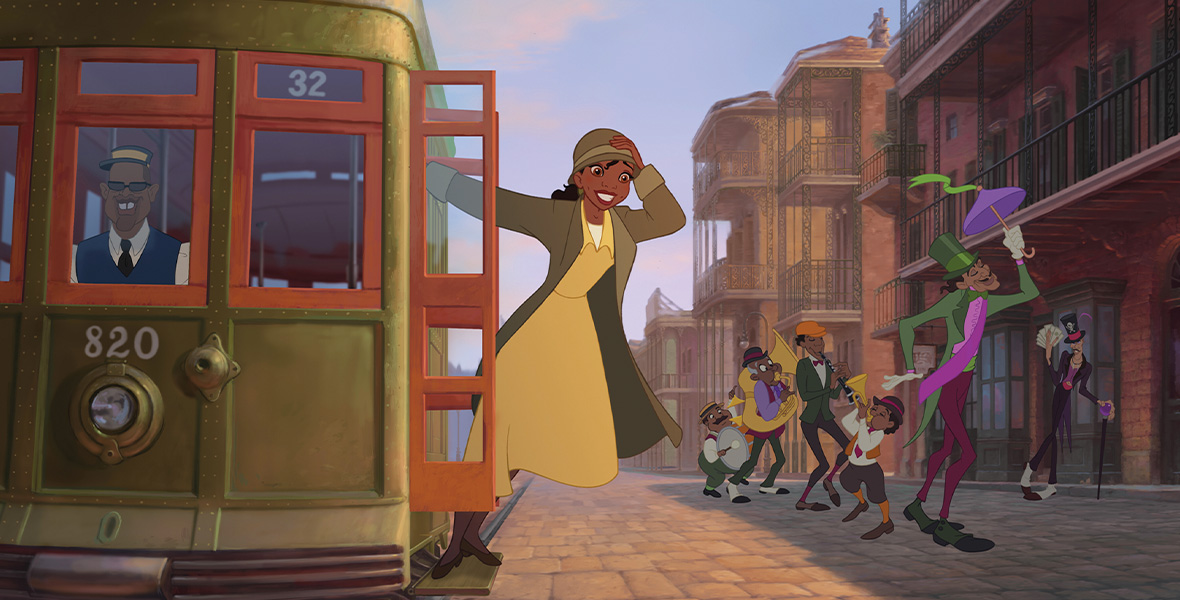 In a scene from The Princess and the Frog, Tiana, an animated young woman, hangs off a railway car with her right arm and holds her green bowler hat with her left hand. She wears a yellow dress and a green overcoat. The railway car is green and brown and cruises down the center of the cobblestone street.
