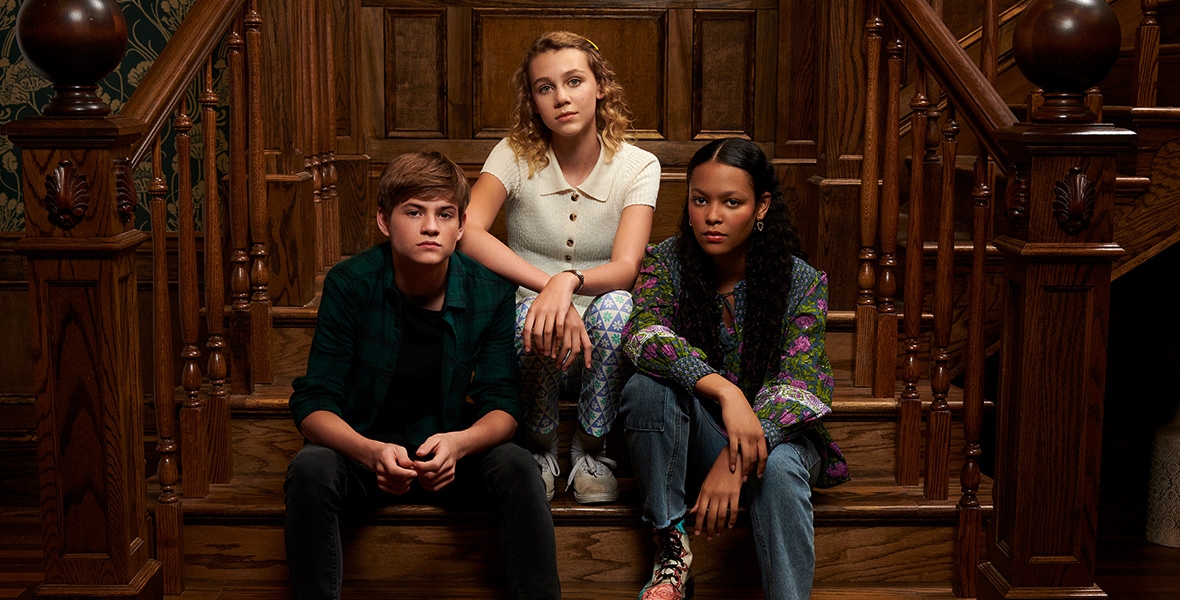 In a promotional photo for Secrets of Sulphur Springs, Preston Oliver, Elle Graham, and Kyliegh Curran are seated on an old wooden staircase. No one is smiling.