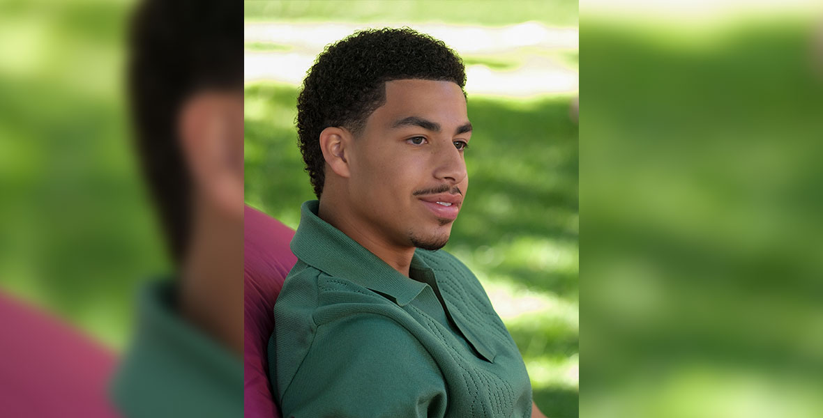 In a scene from grown-ish, actor Marcus Scribner as Junior sits in a cardinal hammock on green grass and wears a green, button-down shirt.