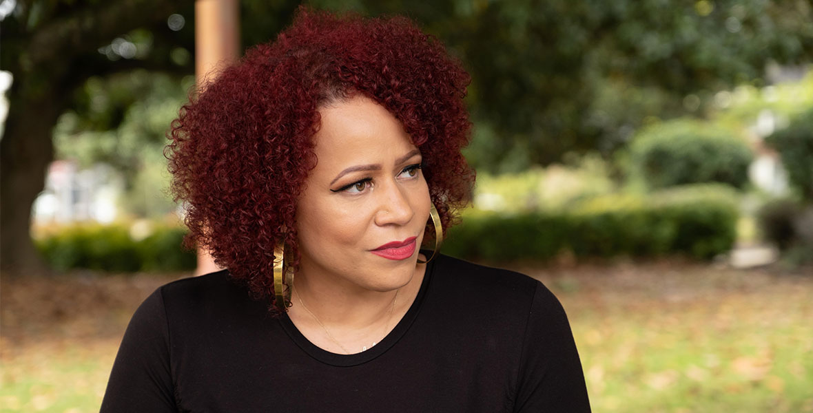 In a scene from The 1619 Project, host and creator Nikole Hannah-Jones sits in a chair and wears a black, long-sleeved shirt. 