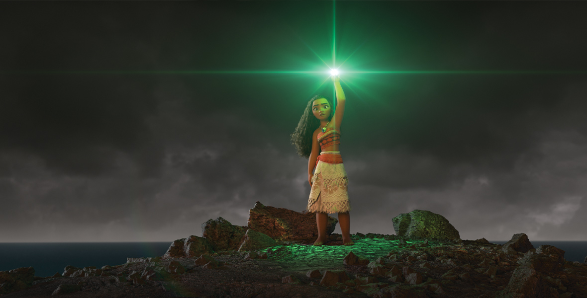 Under a dark, cloudy sky, Moana stands alone atop a rock. She has animated flowing dark hair and wears a red, strapless top and a tan, knee-length skirt. She raises her left arm sky-high, and the heart of Te Fiti shines within her hand. The heart glows green, glimmering brightly under the gloomy sky.