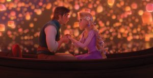 In the animated film Tangled, Rapunzel and Eugene sit in a small boat together as they hold hands and look into each other’s eyes. Rapunzel’s blond hair is braided back with vibrant flowers, and she wears a purple dress with small, puffed sleeves. Eugene wears a white long-sleeved shirt with a green vest. Behind them, the night sky is lit up with hundreds of glowing lanterns that float above them and drift on the water.