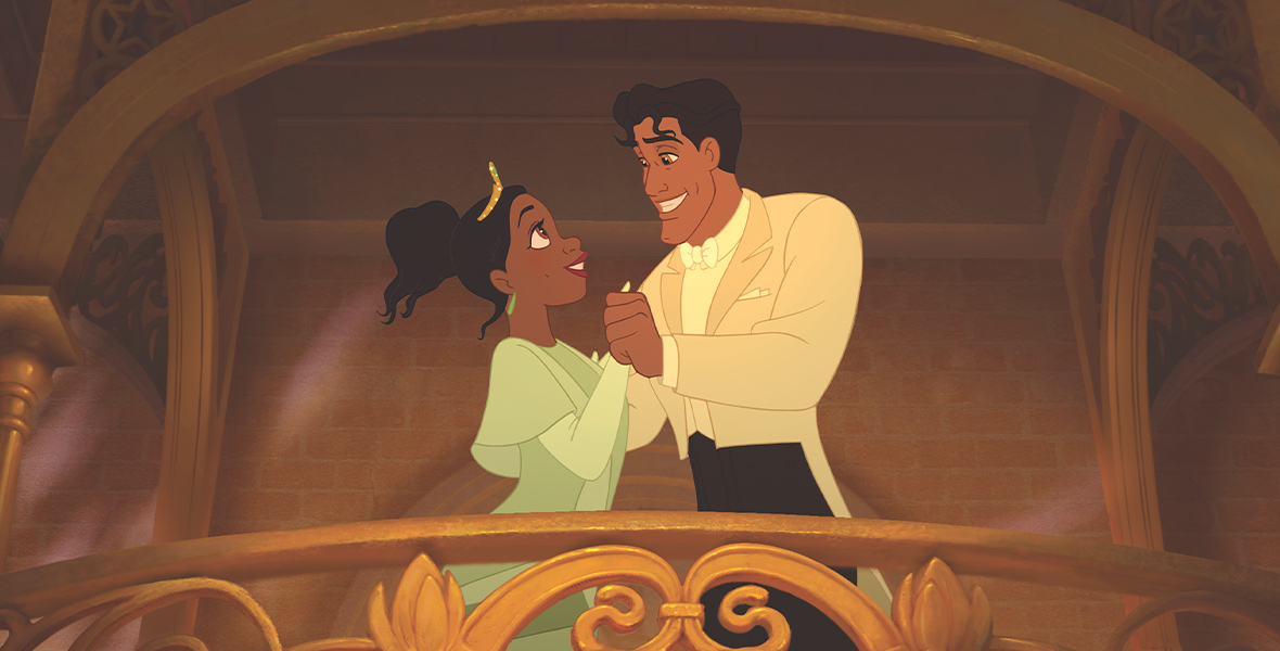 In the animated film The Princess and the Frog, Tiana and Naveen dance on the gold balcony of Tiana’s Palace. Tiana wears a green dress, gloves, and a gold tiara, while Naveen wears a white suit with black pants. They grin at each other.