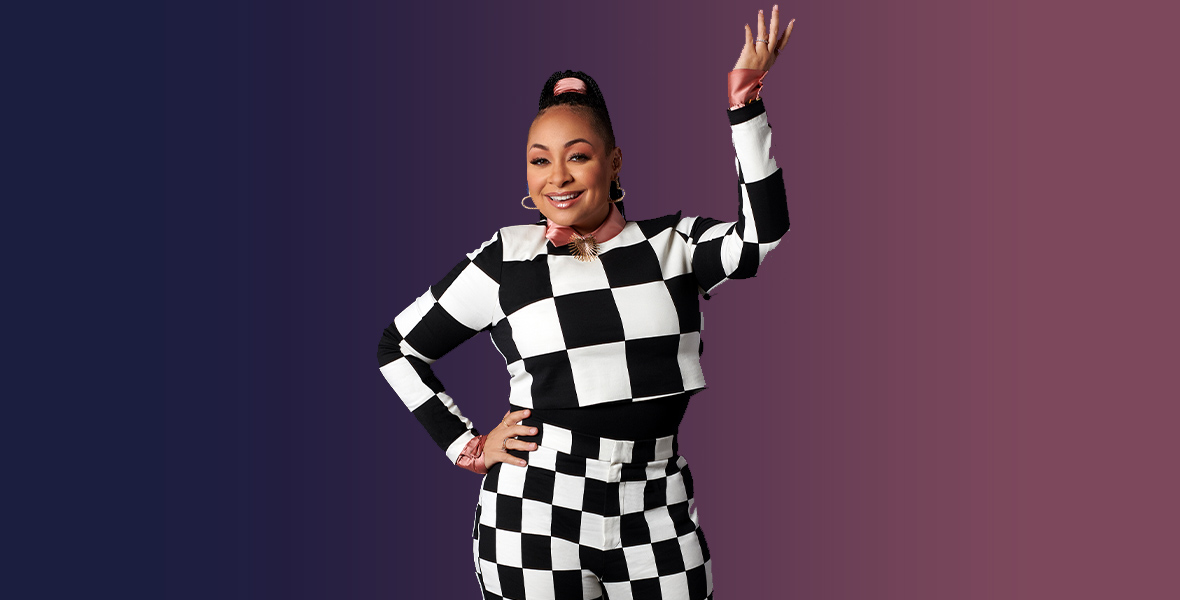 In a promotional photo for Raven’s Home, Raven-Symoné wears a black and white checkered sweater and matching pants. She is wearing a silk pink shirt and a matching pink silk ribbon in her hair. She is accessorized with gold hoop earrings and rings. She is smiling and posing with one hand on her hip and the other bent upward.