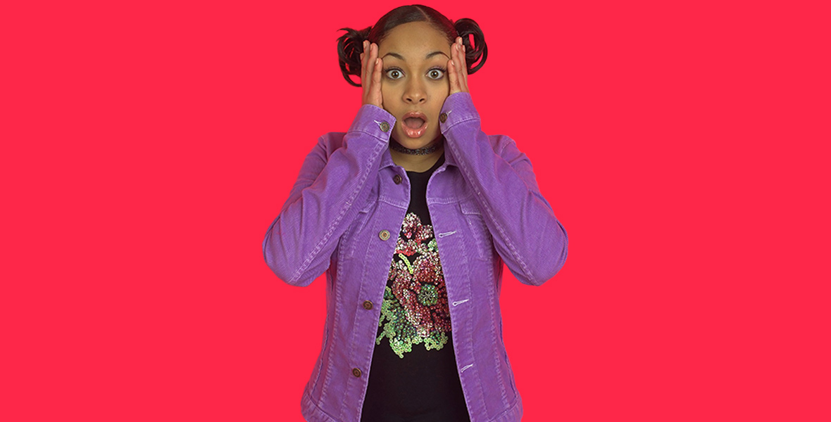 In a promotional photo for That’s So Raven, Raven-Symoné’s eyes are wide-open and her mouth is agape. Her hands are on both sides of her face. She is wearing a purple corduroy jacket, a black shirt featuring a bedazzled flower, and a lacy choker.