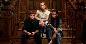 Preston Oliver, Elle Graham, and Kyliegh Curran sit on a wooden staircase on the set of Secrets of Sulphur Springs.