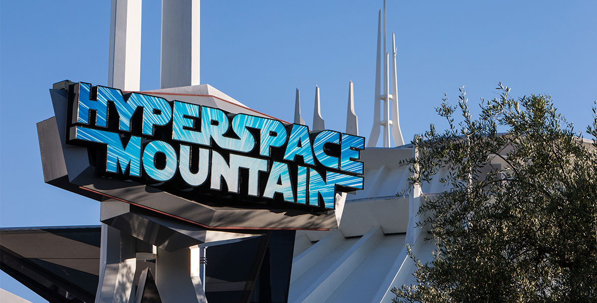 The sign outside of Hyperspace Mountain, the Star Wars version of Space Mountain at Disneyland Park. The spires of Space Mountain are seen behind the sign, which features letters made up of the “lightspeed” effect from the Star Wars films.