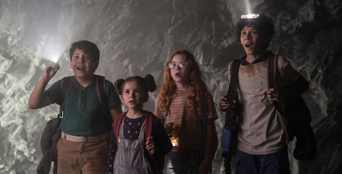 In a scene from Journey to the Center of the Earth, four children use various types of flashlights to see in a cave. Each of the kids has an awestruck expression.