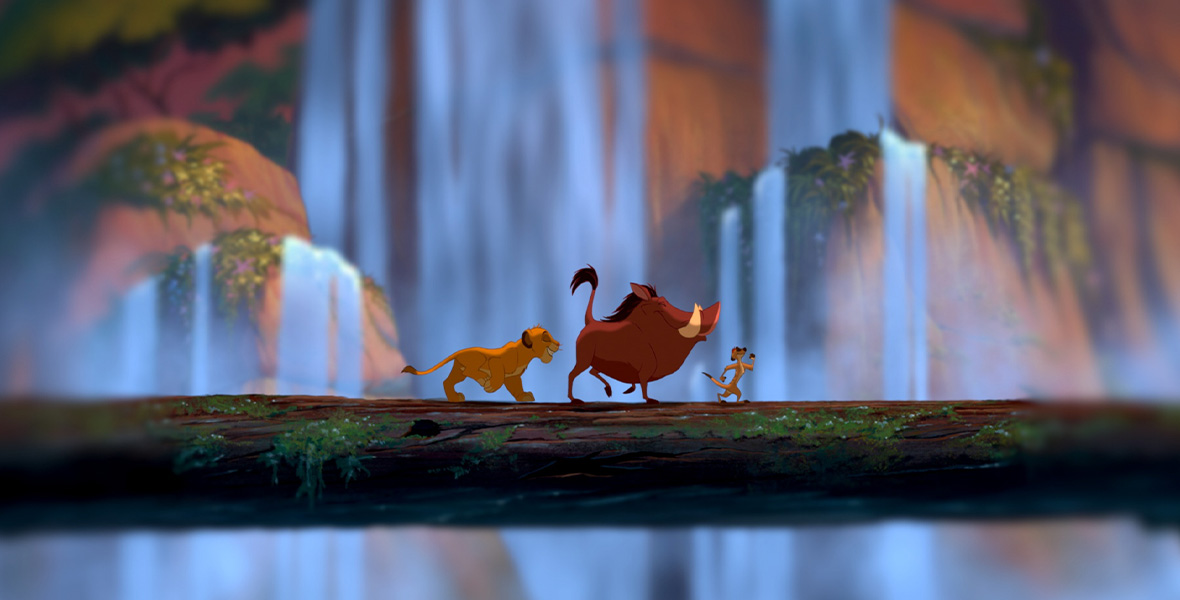 In a still from the animated film The Lion King, Timon the meerkat, Pumbaa the warthog, and Simba the lion strut in a single file line across a mossy log. Waterfalls flow behind them.