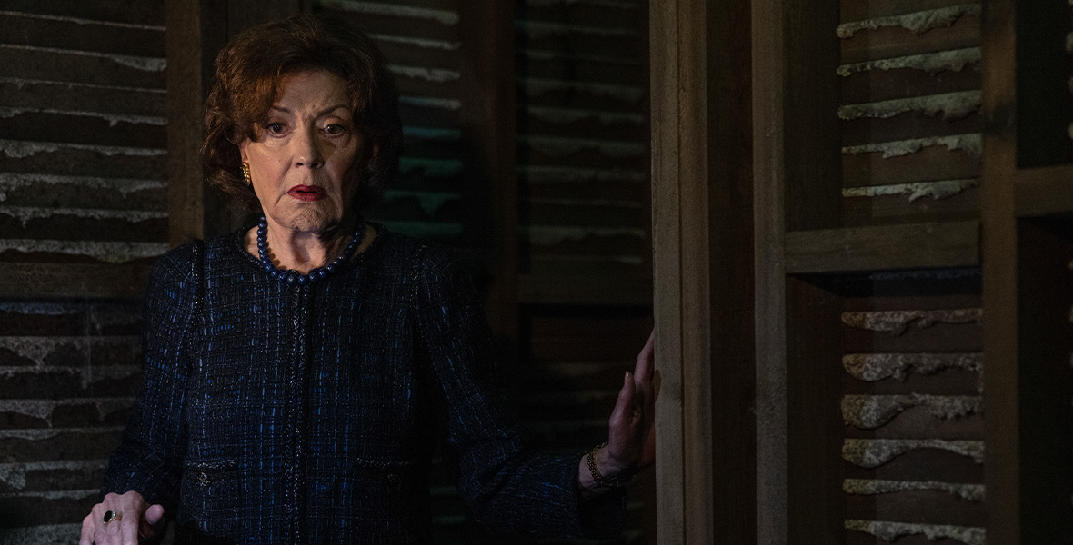 In a scene from an episode of The Watchful Eye, actor Kelly Bishop wears a black pantsuit and stands in a dark basement.