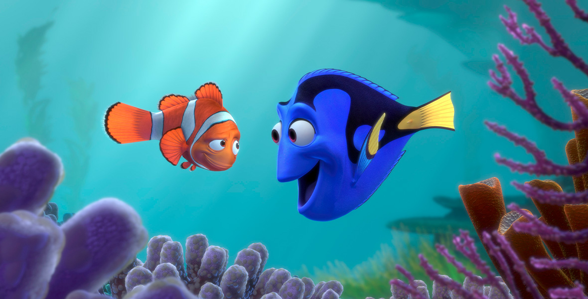 In a still from the animated film Finding Nemo, Marlin the clownfish and Dory the blue tang look mischievously at one another. Marlin, orange with white stripes, looks skeptical while the blue Dory grins with wide eyes. In the cyan ocean, purple coral pokes up beneath them.