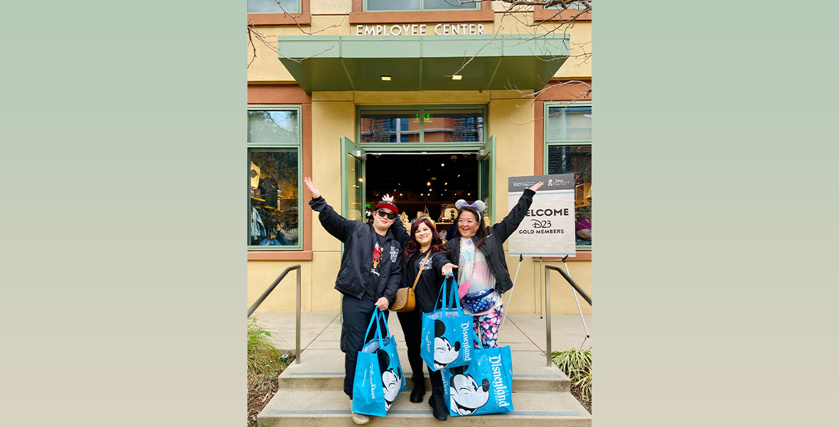 D23 Gold Members stand in front of the employee store with lots of blue Mickey Mouse shopping bags full of their new merchandise.