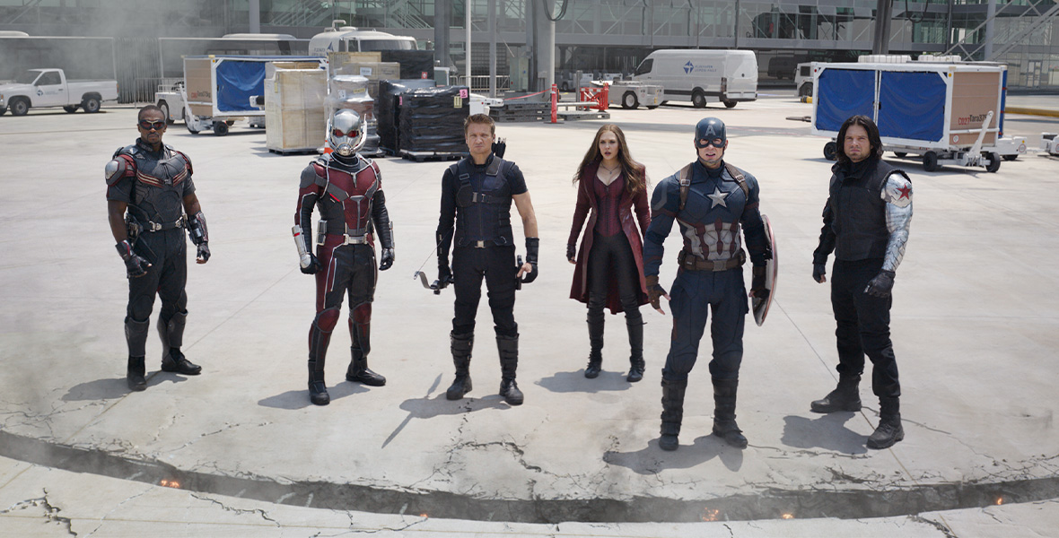 In a still of Captain America: Civil War, six Super Heroes stand on the concrete and stare up at the sky. Among them are Captain America, the Winter Soldier, Scarlet Witch, Hawkeye, Ant-Man, and the Falcon. They’re all dressed in their fighter gear.