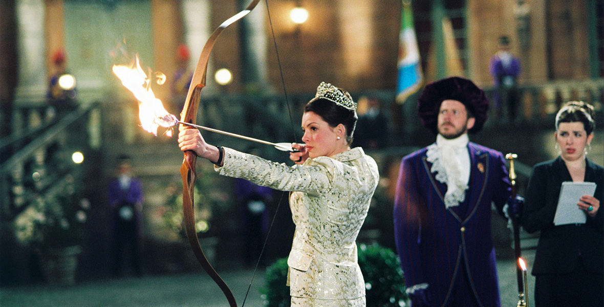 In a scene from The Princess Diaries 2: Royal Engagement, actor Anne Hathaway shoots a flaming arrow and wears a silver crown atop her head and a white and silver pantsuit.