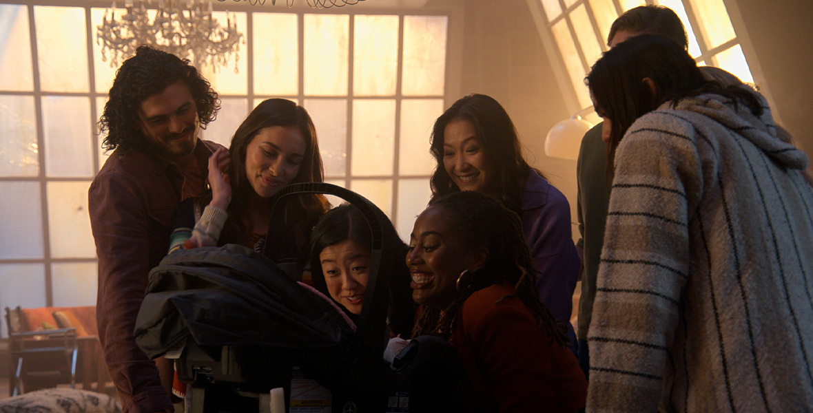 In a scene from an episode of Good Trouble, actors Tommy Martinez, Priscilla Quintana, Sherry Cola, Zuri Adele, and Kara Wang gather around a baby’s car seat.