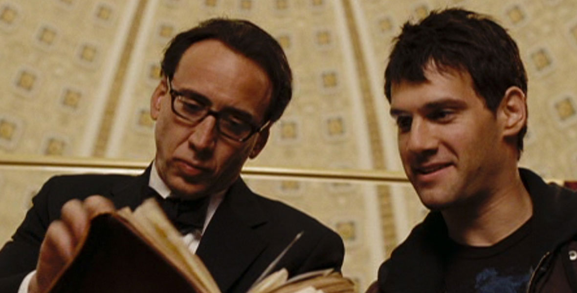 In a scene from National Treasure: Book of Secrets, actors Nicolas Cage and Justin Bartha gather around a large antique book.
