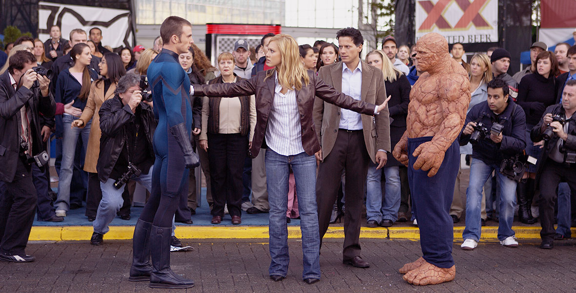 In a scene from Fantastic Four (2005), actor Jessica Alba separates actors Chris Evans and Michael Chiklis from fighting in front of a crowd as actor Ioan Gruffudd stands behind Alba.