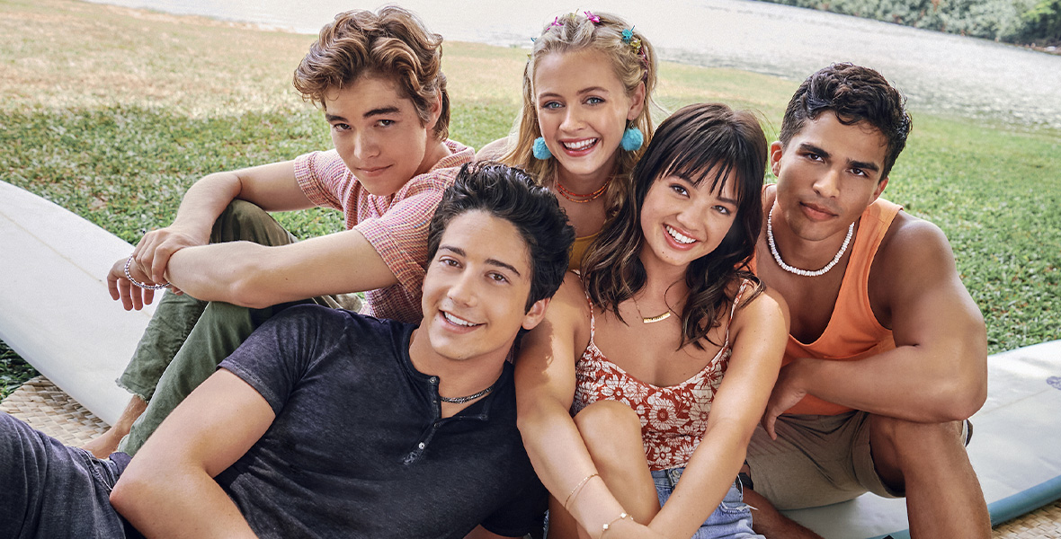 In a promotional image for Doogie Kamealoha, M.D., actors Matthew Sato, Milo Manheim, Emma Meisel, Peyton Elizabeth Lee, and Alex Aiono smile and sit huddled together on a grass lawn.