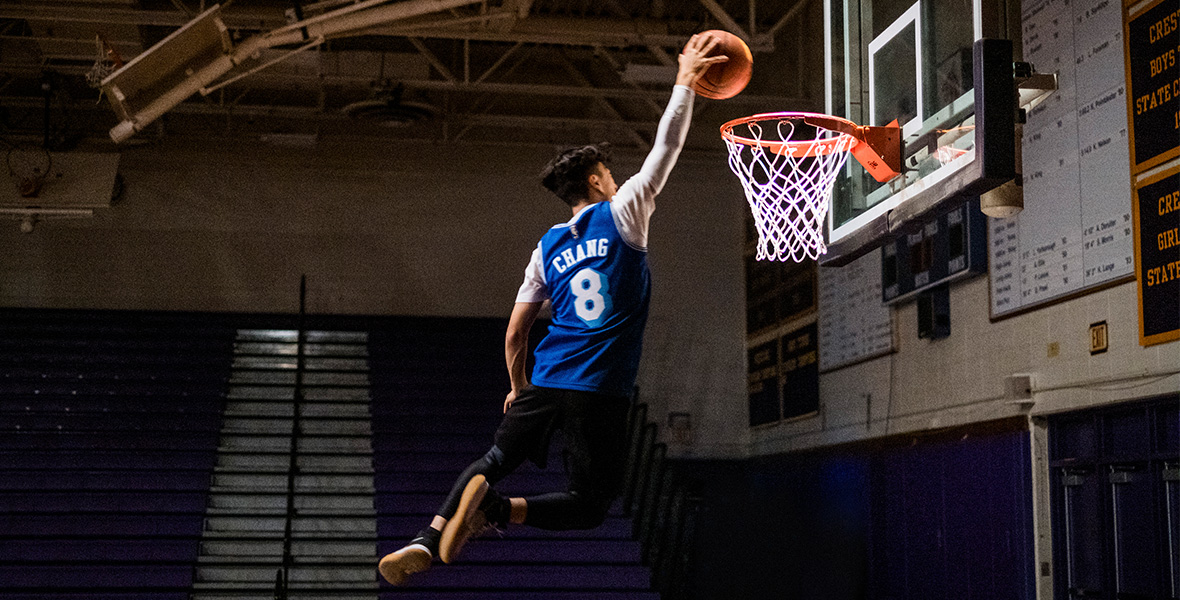 In a scene from Chang Can Dunk, actor Bloom Li dunks an orange basketball and wears a blue jersey reading “Chang,” with the number “8” on the back.