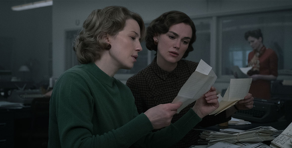In a scene from Boston Strangler, actors Carrie Coon and Keira Knightley sit at a desk and look at small pieces of paper.
