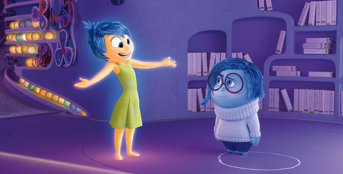 In the animated film Inside Out, Joy and Sadness stand inside the colorful Headquarters, a shelf of purple manuals behind them. Sadness looks glum as usual, while Joy throws her arms out and smiles at her.