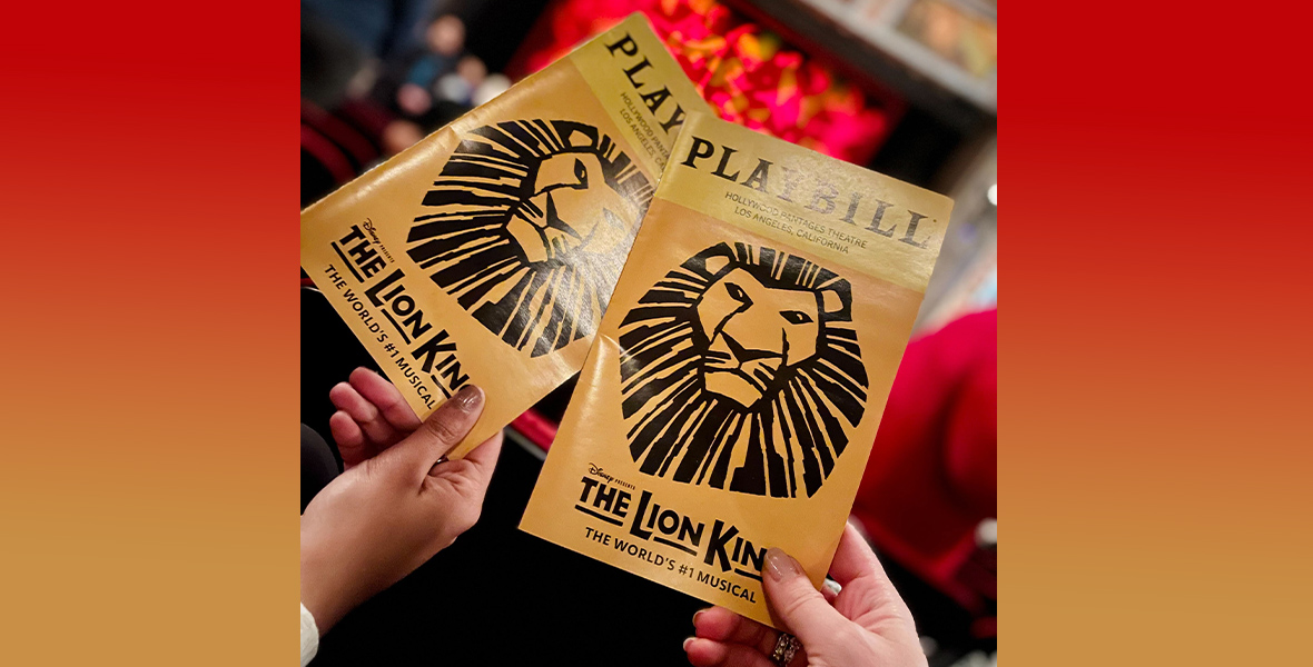 Enthusiastic audience members hold up their iconic yellow playbills in front of The Lion King stage at the Hollywood Pantages.