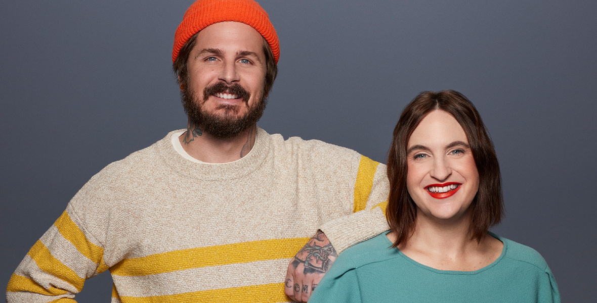 A photo of Kiff’s creators, Nic and Lucy, who smile at the camera. Wearing an orange beanie and yellow striped sweater, Nic rests his elbow on Lucy’s shoulder. Lucy wears a cyan top.