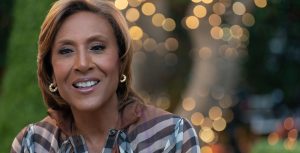 Robin Roberts wears a Burberry shirt, a gold necklace, and gold earrings.