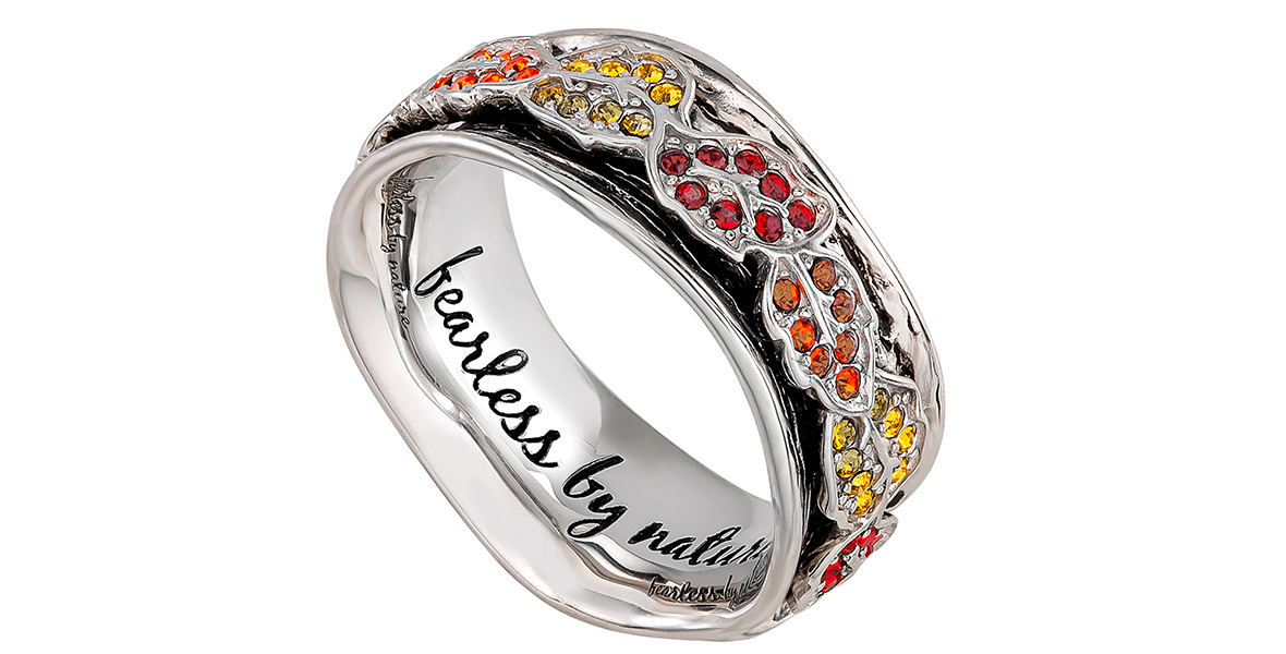A silver ring encircled by silver leaves. Each leaf is decorated with either yellow, orange, or red jewels. The phrase “Fearless by nature” is engraved in cursive on the inside of the ring.